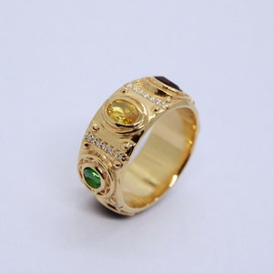 May include: A gold band ring with three oval-shaped gemstones. The ring is set with a yellow, green, and red gemstone. The ring is decorated with small diamonds.