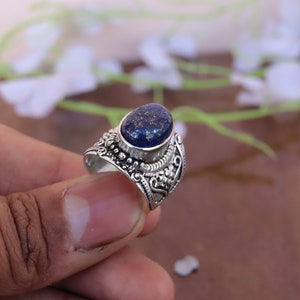 May include: A silver ring with an oval-shaped lapis lazuli gemstone. The ring has an intricate, ornate design.