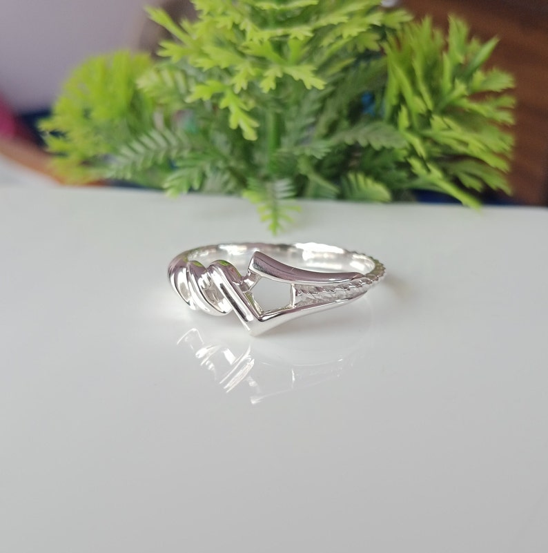 May include: A silver ring with a twisted band and a unique open design. The ring is made of polished silver and has a smooth finish.
