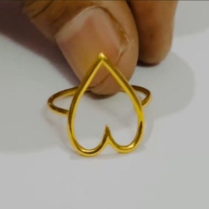 Puede incluir: Un anillo de color dorado con un diseño en forma de corazón. El anillo está hecho de un metal delgado y tiene un aspecto simple y elegante.