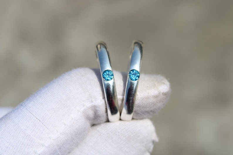 May include: Two silver rings with a blue gemstone set in each. The rings are held in a white cloth.