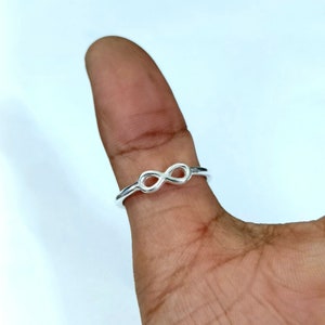 Könnte beinhalten: Ein silberner Unendlichkeitsring an einem Finger.