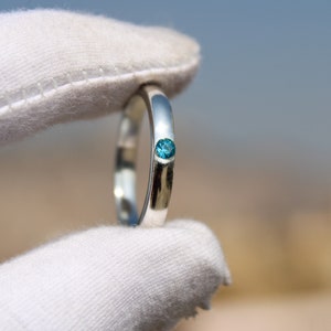 May include: A silver ring with a single, small, blue gemstone set in the band.