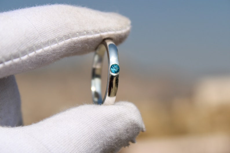 May include: A silver ring with a single, small, blue gemstone set in the band.