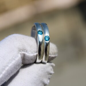 May include: Two silver rings with blue gemstones set into the bands.