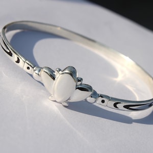 Könnte beinhalten: Ein silbernes Armreif-Armband mit einem Schmetterlingsanhänger und einem schwarz-weißen Design.