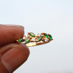 Puede incluir: Un anillo de oro con un diseño delicado que presenta piedras preciosas verdes y blancas. El anillo está engastado con pequeñas piedras verdes en forma de marquesa y piedras blancas redondas, creando un patrón de hojas.