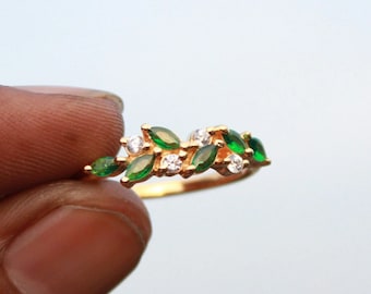 May include: A gold ring with a delicate design featuring green and white gemstones. The ring is set with small, marquise-shaped green stones and round white stones, creating a leafy pattern.