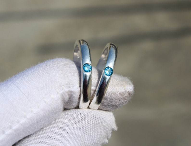 May include: Two silver rings with a small blue gemstone set in each. The rings are held together by a white cloth.