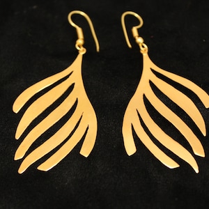 May include: A pair of gold-toned earrings with a feather-like design. The earrings are made of metal and have a delicate, intricate pattern.