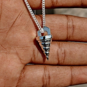 Puede incluir: Collar con colgante plateado con diseño de broca. El colgante, suspendido de una cadena plateada, tiene forma cónica con ranuras en espiral. El collar se muestra sobre un fondo neutro. La cadena es de plata.