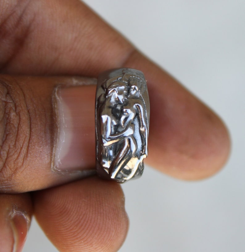 May include: A silver ring with a detailed sculpture of two figures embracing.