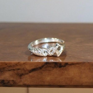 May include: A silver ring with a braided design and a heart-shaped cutout in the center.