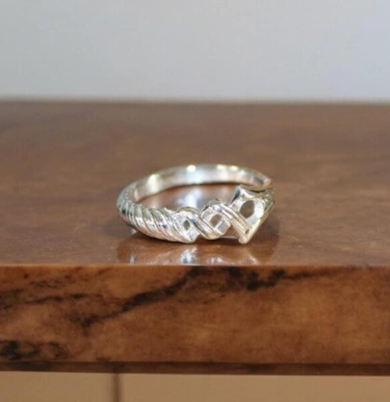 May include: A silver ring with a braided design and a heart-shaped cutout in the center.