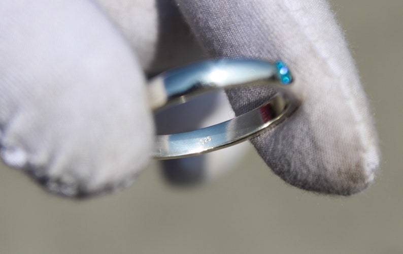 May include: A silver ring with a blue gemstone set in the band. The ring is marked with the number "925" on the inside.
