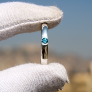 May include: A silver ring with a single, small, blue gemstone set in the center.