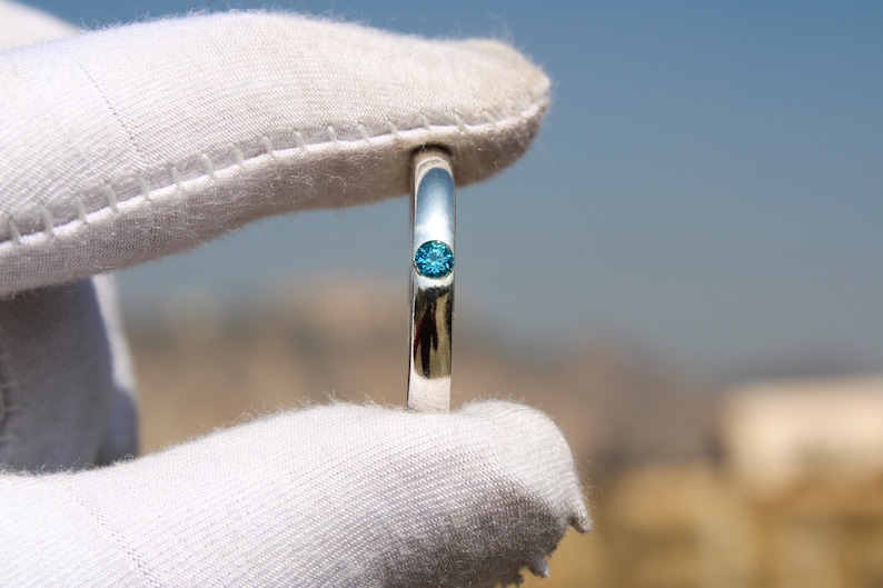May include: A silver ring with a single, small, blue gemstone set in the center.