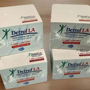 May include: Four white boxes of Detrol LA tolterodine tartrate extended release capsules are stacked. Each box has the product name, dosage information, and a green and blue logo. The boxes are wrapped in clear plastic.