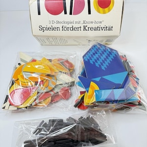 May include: A vintage "Pablo" 3D puzzle game box with the text "hat 120 Teile". The box is white with the word "Pablo" in large, colorful letters. The game includes various colorful geometric shapes and black connecting pieces.