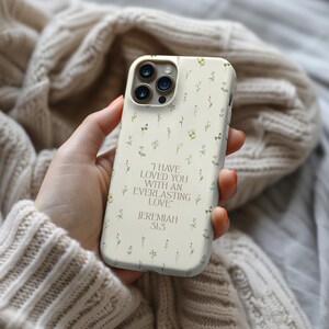 May include: A cream-coloured phone case with a floral pattern and the quote "I HAVE LOVED YOU WITH AN EVERLASTING LOVE" from Jeremiah 31:3. The case features small green, yellow, and purple flowers.