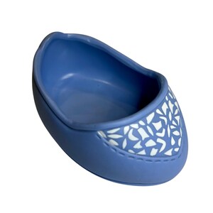 May include: A blue decorative shoe-shaped dish. The dish has a rounded shape with a white floral pattern on the front. The dish is made of a smooth material and has a stitched detail.