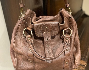 May include: A brown leather handbag with a flap closure and multiple metal studs. The bag has two top handles and a shoulder strap.