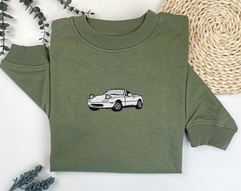 May include: A green sweatshirt with a white embroidered image of a convertible car.