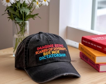 May include: A black baseball cap with a distressed look. The cap has a rainbow-colored embroidered message that reads "Imagine being scared of diversity, but not dictatorship."