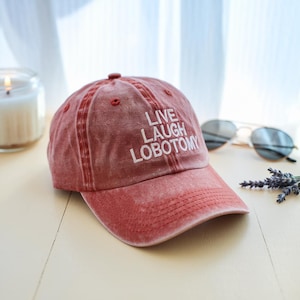 May include: A red distressed baseball cap with white embroidered text that reads "Live Laugh Lobotomy".