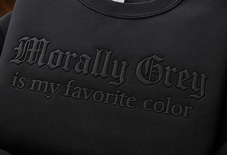 K&ouml;nnte beinhalten: Schwarzes Sweatshirt mit dem gestickten Schriftzug "Morally Grey is my favorite color" in einer gotischen Schriftart. Der Text ist farblich auf den dunklen Stoff abgestimmt.
