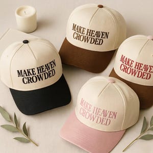 May include: Four baseball caps with cream-coloured crowns and contrasting brims in black, dark brown, maroon, and light pink. Each cap features the embroidered text "MAKE HEAVEN CROWDED" in a matching thread colour on the front panel of the crown.