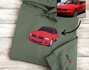 May include: A green hooded sweatshirt with a red car embroidered on the front. The car is a convertible and has a black interior. The sweatshirt also has the name "Adam" embroidered on the sleeve with a red heart.