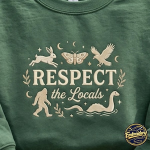 May include: A forest green sweatshirt featuring cream-colored embroidery of a rabbit, moth, bird, Bigfoot, and a sea creature. The text reads RESPECT the Locals, surrounded by small stars, moons, and leafy sprigs in a circular arrangement.