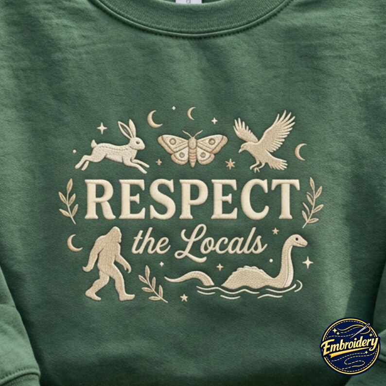 May include: A forest green sweatshirt featuring cream-colored embroidery of a rabbit, moth, bird, Bigfoot, and a sea creature. The text reads RESPECT the Locals, surrounded by small stars, moons, and leafy sprigs in a circular arrangement.