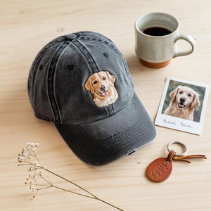 Peut inclure: Casquette de baseball gris anthracite vieilli avec une broderie de golden retriever. Une photo polaroid d'un golden retriever, un porte-clés en cuir et une tasse de café sont également présents.