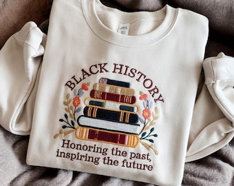 May include: A cream-colored sweatshirt with an embroidered design of a stack of books with the words "Black History" above the books and "Honoring the past, inspiring the future" below the books.