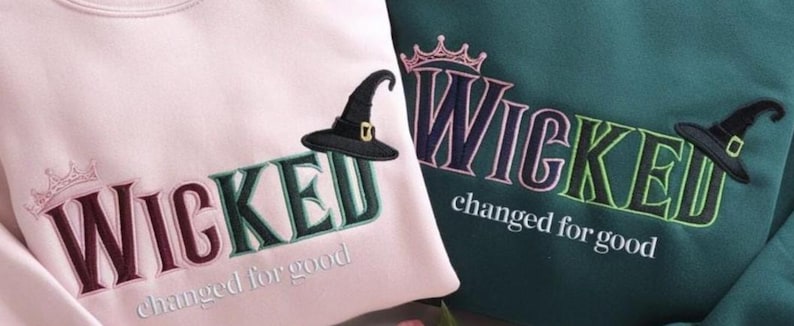 Puede incluir: Dos sudaderas, una rosa y otra verde azulado, bordadas con la palabra "WICKED" en una fuente estilizada. Cada sudadera presenta un sombrero de bruja y la frase "changed for good". Una corona est&aacute; bordada encima de la palabra "WICKED".