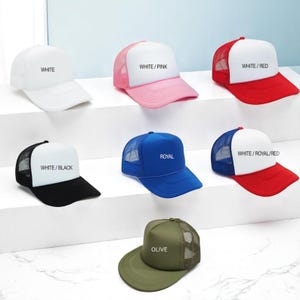 May include: Seven trucker caps with mesh backs and foam front panels in various colour combinations: white, white/pink, white/red, white/black, royal blue, white/royal/red, and olive. Each cap features a curved brim and a snapback closure.