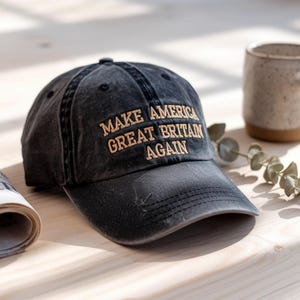 May include: A black baseball cap with a distressed look and the text "Make America Great Britain Again" embroidered in gold.