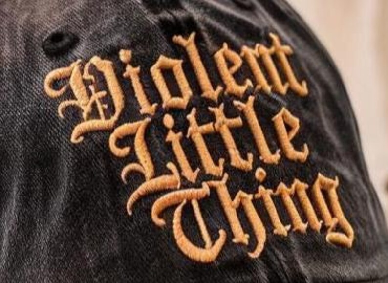 May include: Black baseball cap with the words "Violent Little Thing" embroidered in gold script.