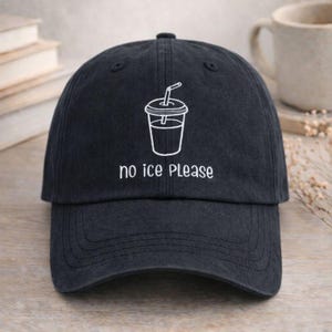 May include: A navy blue baseball cap with a curved peak. The cap has a white graphic of a beverage cup with a straw, and the words "no ice PLEASE" are printed below the graphic in white.