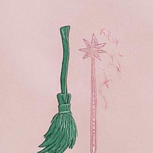 Op de afbeelding: Een lichtroze sweatshirt met geborduurde illustraties van een groene bezem en een roze toverstaf met steraccenten. Het ontwerp heeft een grillig, fantasiethema.