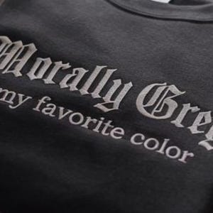 以下が含まれることがあります： ゴシック体で「Morally Grey is my favorite color」と刺繍されたダークグレーのスウェットシャツ。 文字は明るいグレーで、生地とのコントラストを生み出しています。