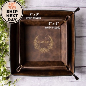 May include: A brown faux leather valet tray with a personalized inscription "HARPER" in gold lettering. The tray is 9 inches by 9 inches when folded and 6 inches by 6 inches when folded.