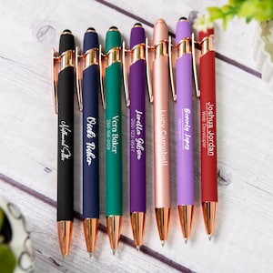 May include: Seven personalised pens with rose gold accents and a stylus tip. The pens are black, navy blue, green, purple, rose gold, lavender, and red. Each pen has a name and job title or phone number engraved on the side.