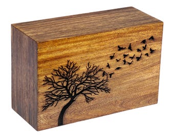 Può includere: Una scatola di legno con un albero e uccelli intagliati nella parte superiore. L'albero è spoglio e gli uccelli stanno volando via. La scatola è di colore marrone scuro.