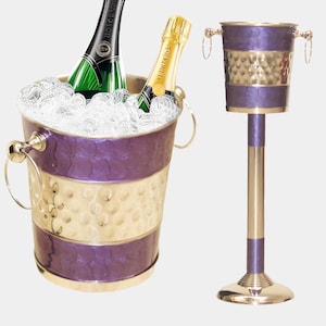May include: A silver champagne bucket with a purple and silver hammered finish, with two bottles of champagne inside, on a matching stand.