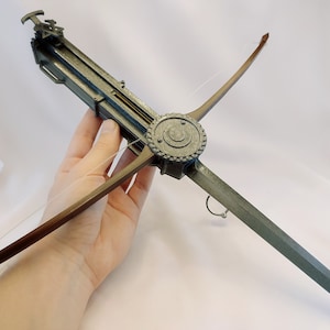 Peut inclure: Arbalète de style antique avec une finition métallique. L'arbalète présente un mécanisme circulaire central, une corde et des bras pointus. La conception comprend des détails complexes, suggérant un thème historique ou fantastique. La palette de couleurs est sourde, avec des nuances de gris et de brun.