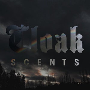May include: A black and white image of the word "Cloak" in a gothic font with a rainbow effect. The word "SCENTS" is written below in a smaller font.