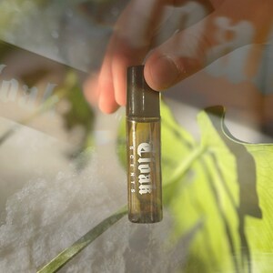 May include: A brown glass bottle with a black cap and the text "Cloak Scents" printed on the label.